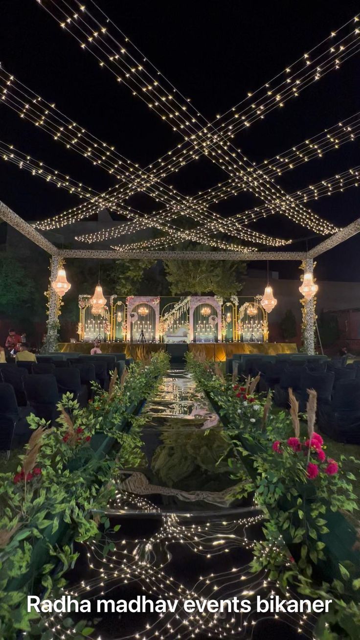 an outdoor event with lights and greenery on the ceiling, surrounded by plants and flowers