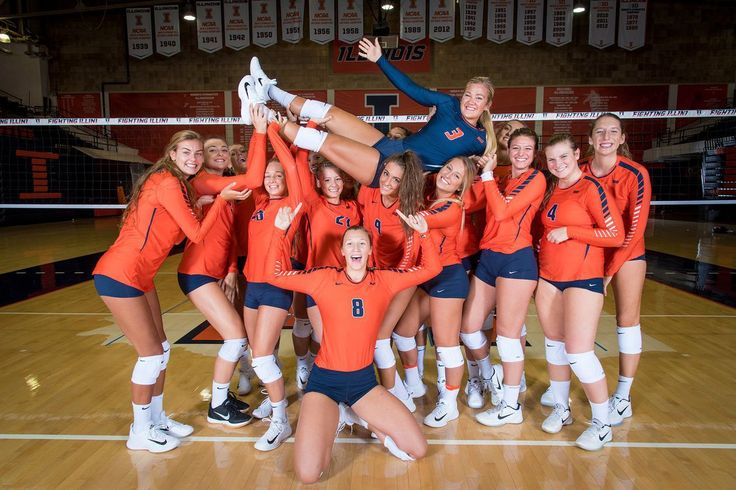 a group of women in orange and blue uniforms posing for a photo on a volleyball court