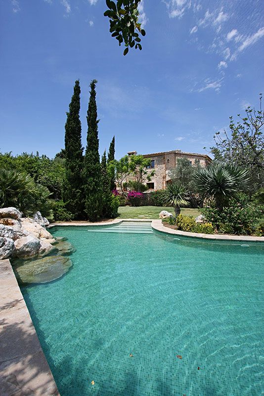 an empty swimming pool surrounded by greenery and stone walls with a house in the background