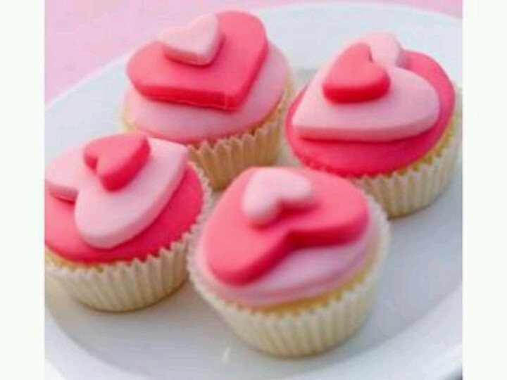 four cupcakes with pink frosting and hearts on them sitting on a white plate