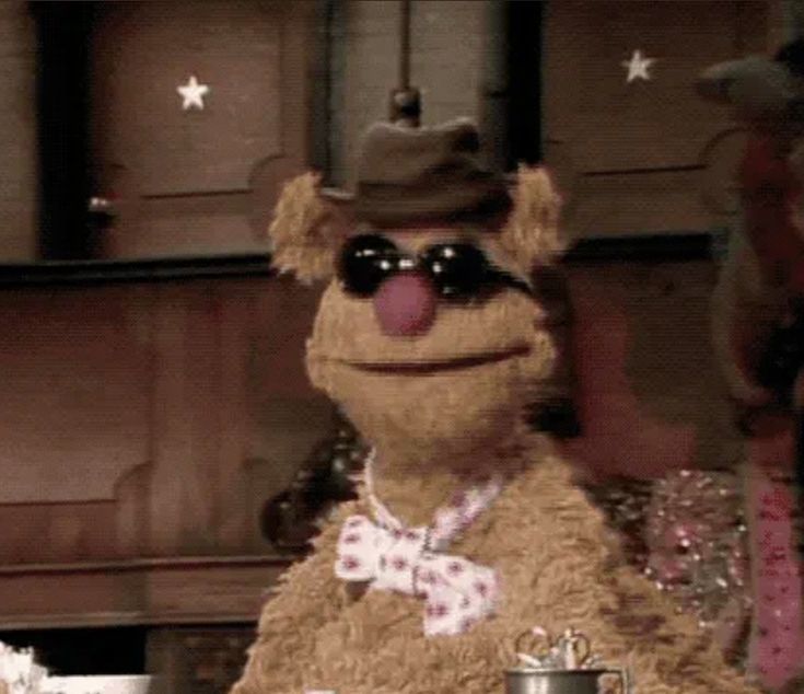 the muppet is wearing sunglasses and a bow tie sitting at a table with other items