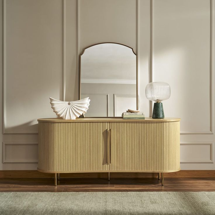 a large mirror sitting on top of a wooden cabinet next to a lamp and vase