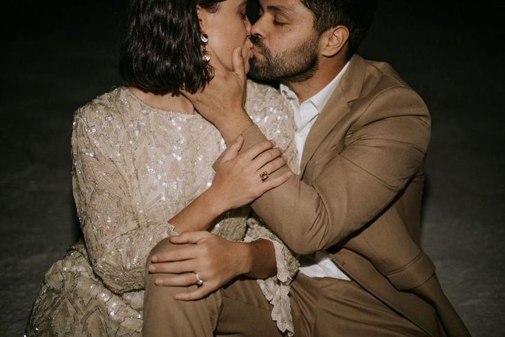 a man and woman kissing each other in front of a dark background with their eyes closed