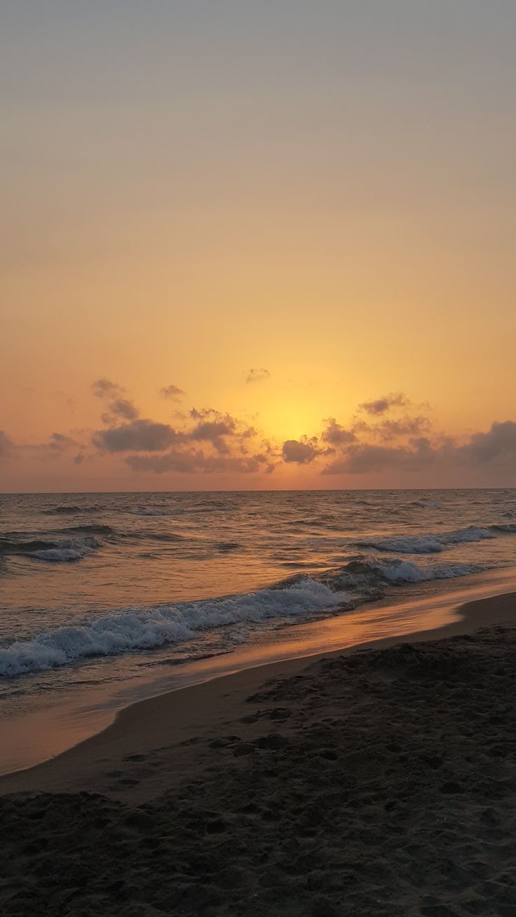 the sun is setting over the ocean with waves coming in