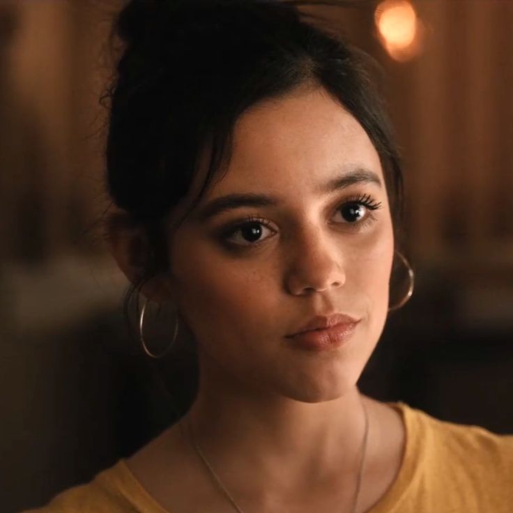 a close up of a person wearing large hoop earrings and a t - shirt with lights in the background