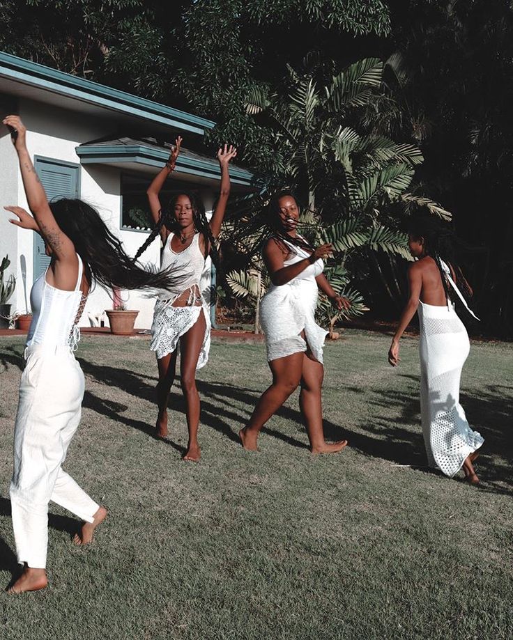 four women in white dresses are dancing on the grass