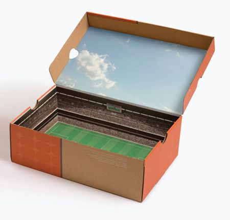 an open cardboard box with the lid opened to reveal a soccer field and sky in it