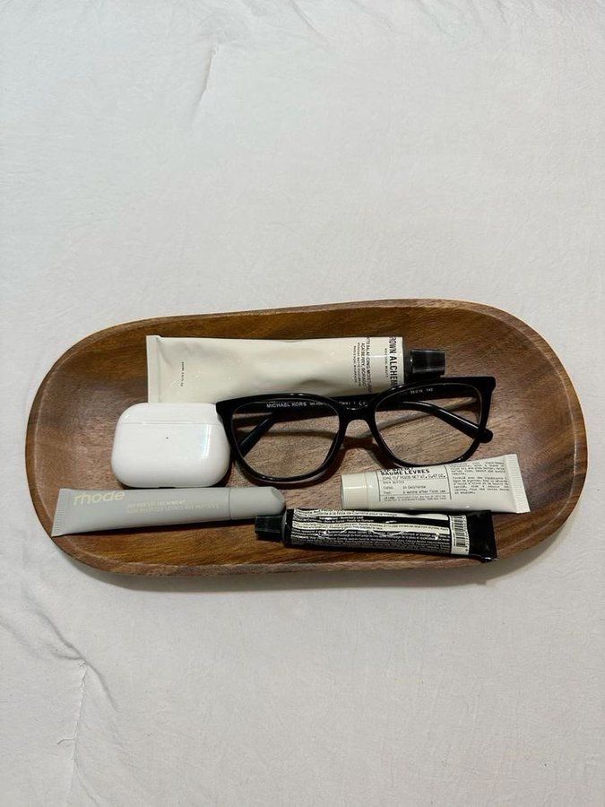 an eyeglasses, toothpaste and other items are arranged on a wooden tray