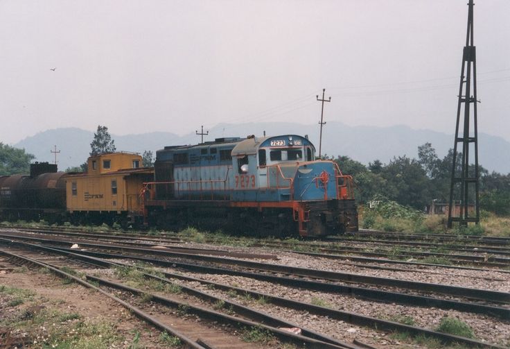 an old blue and yellow train is on the tracks near some power poles, with mountains in the background