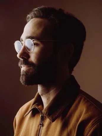 a man with glasses on his face looking off to the side in front of a dark background