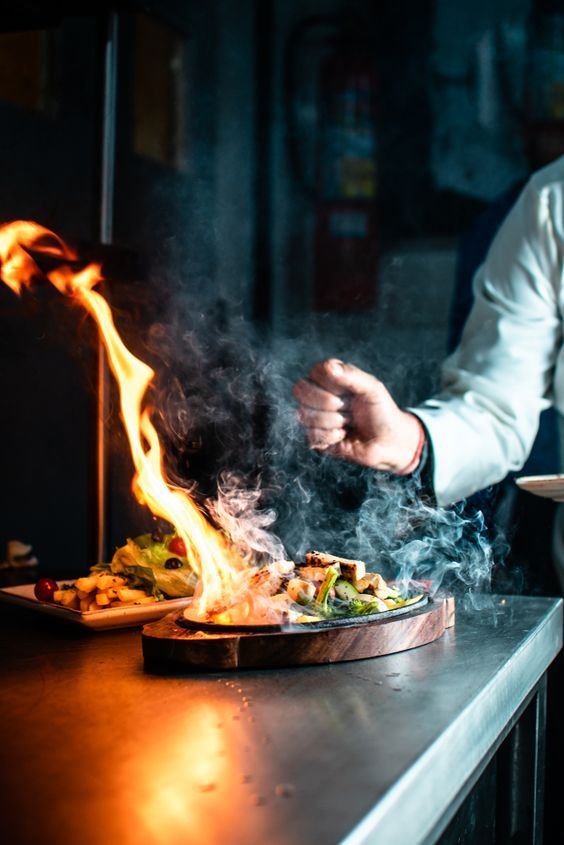 a man cooking food on top of a grill with flames coming out of his hands