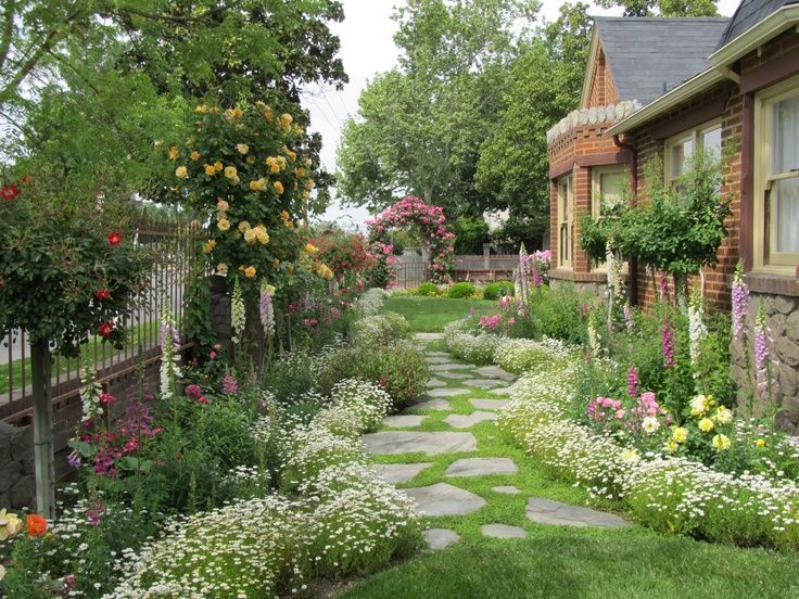 a stone path between two houses with flowers on each side