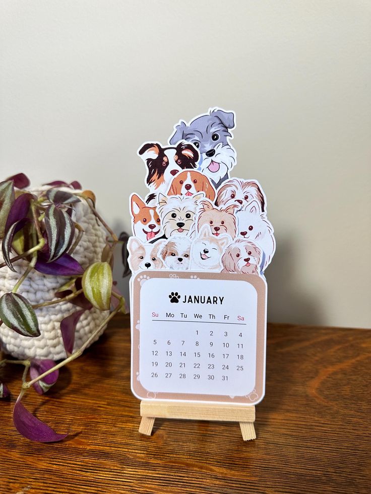 a desk calendar with dogs on it next to a potted plant