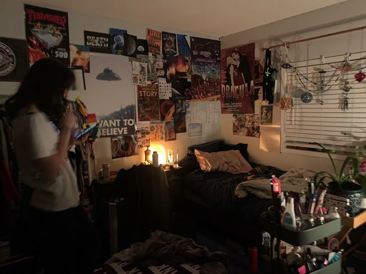 a woman standing in a bedroom next to a bed with lots of posters on the wall