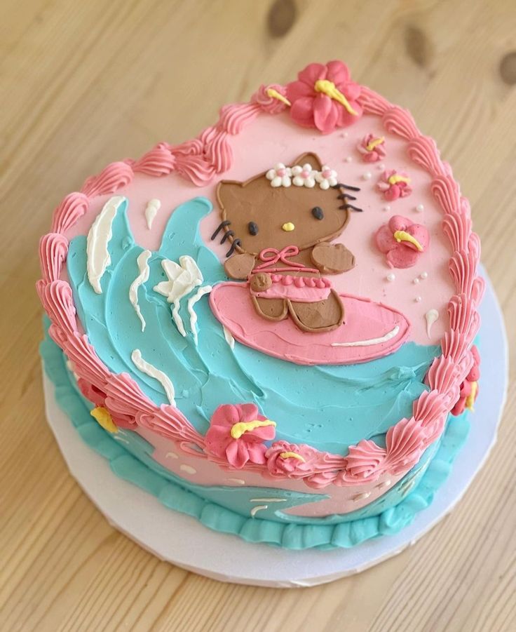 a hello kitty birthday cake with pink and blue frosting on a plate, sitting on a wooden table