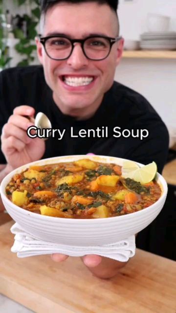 a man holding a bowl of soup in his hand and smiling at the camera, with text overlay that reads curry lentil soup