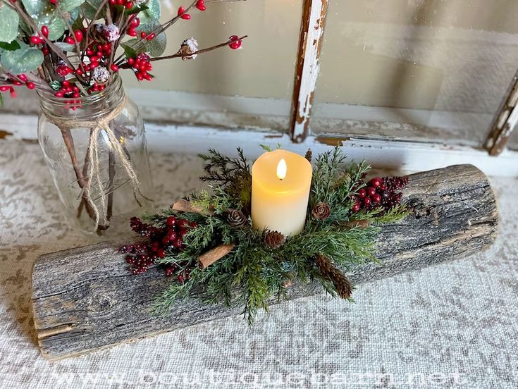 a candle is sitting on a piece of wood next to a vase with red berries and greenery