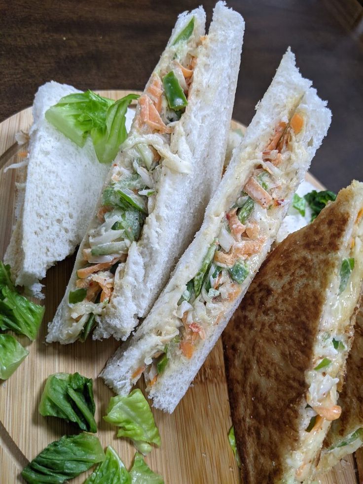 three sandwiches on a wooden plate with lettuce and carrots next to them