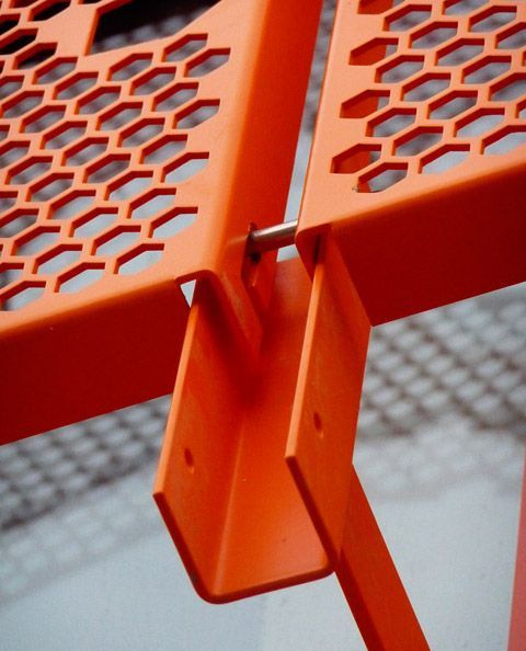 an orange metal bench with holes in the middle and one section missing from it's seat