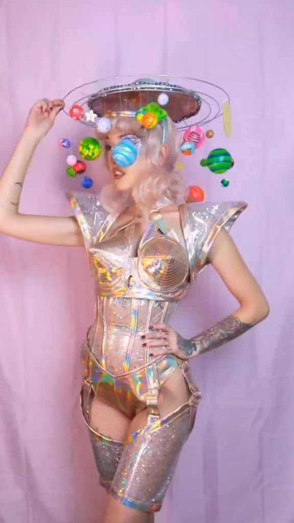 a woman in silver bodysuit with planets on her head and hands behind her head