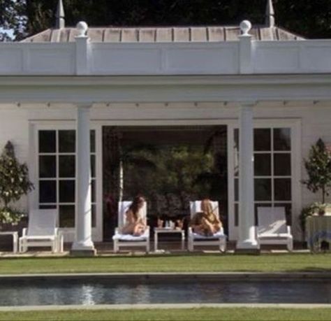 two women lounging on lawn chairs in front of a white house with large windows