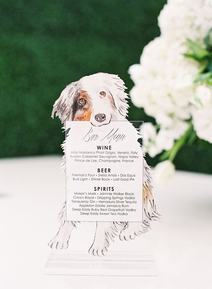 a white and brown dog standing on top of a table next to a vase filled with flowers