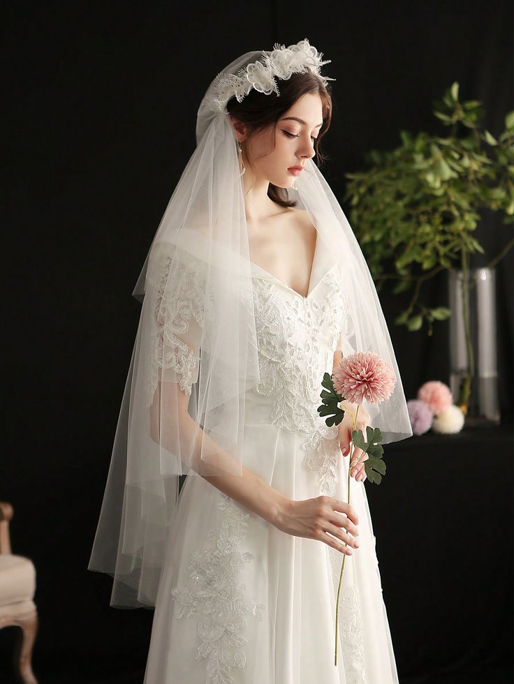 a woman in a white wedding dress holding a flower and wearing a bridal veil