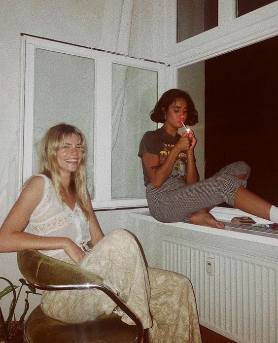 two women are sitting on the windowsill and one is brushing her teeth while the other looks out the window