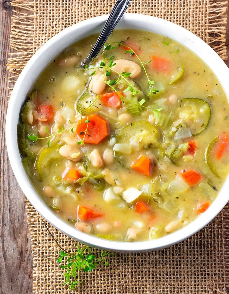 a white bowl filled with vegetable zucchini soup on top of a wooden table