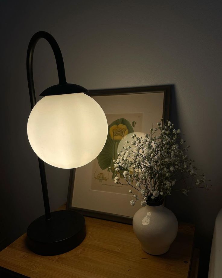 a white vase sitting next to a lamp on top of a wooden table