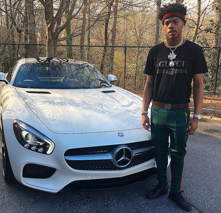 a man standing next to a white sports car in front of a chain link fence