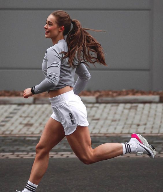 a woman running on the street with her hair blowing in the wind and wearing white shorts