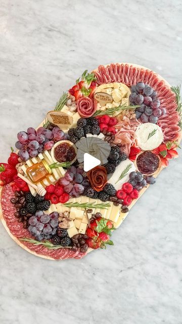 a platter filled with cheese, fruit and meats on top of a marble counter