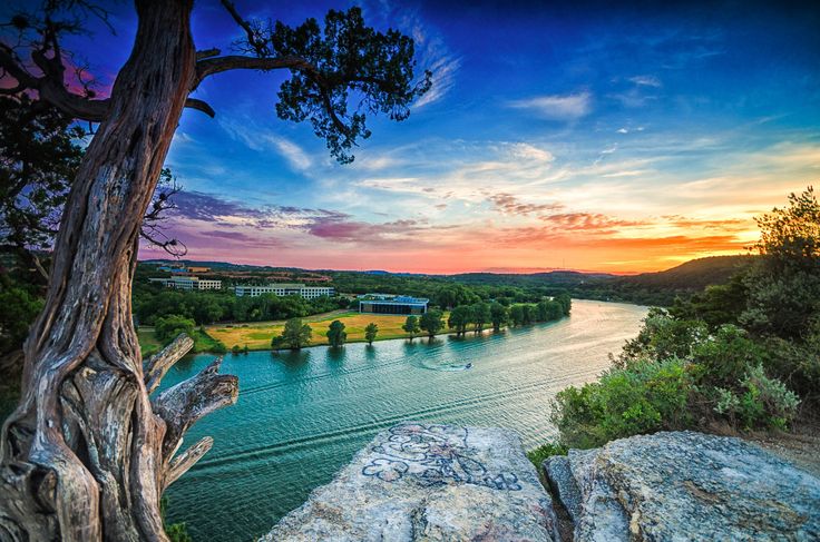 the sun is setting over a river and some trees