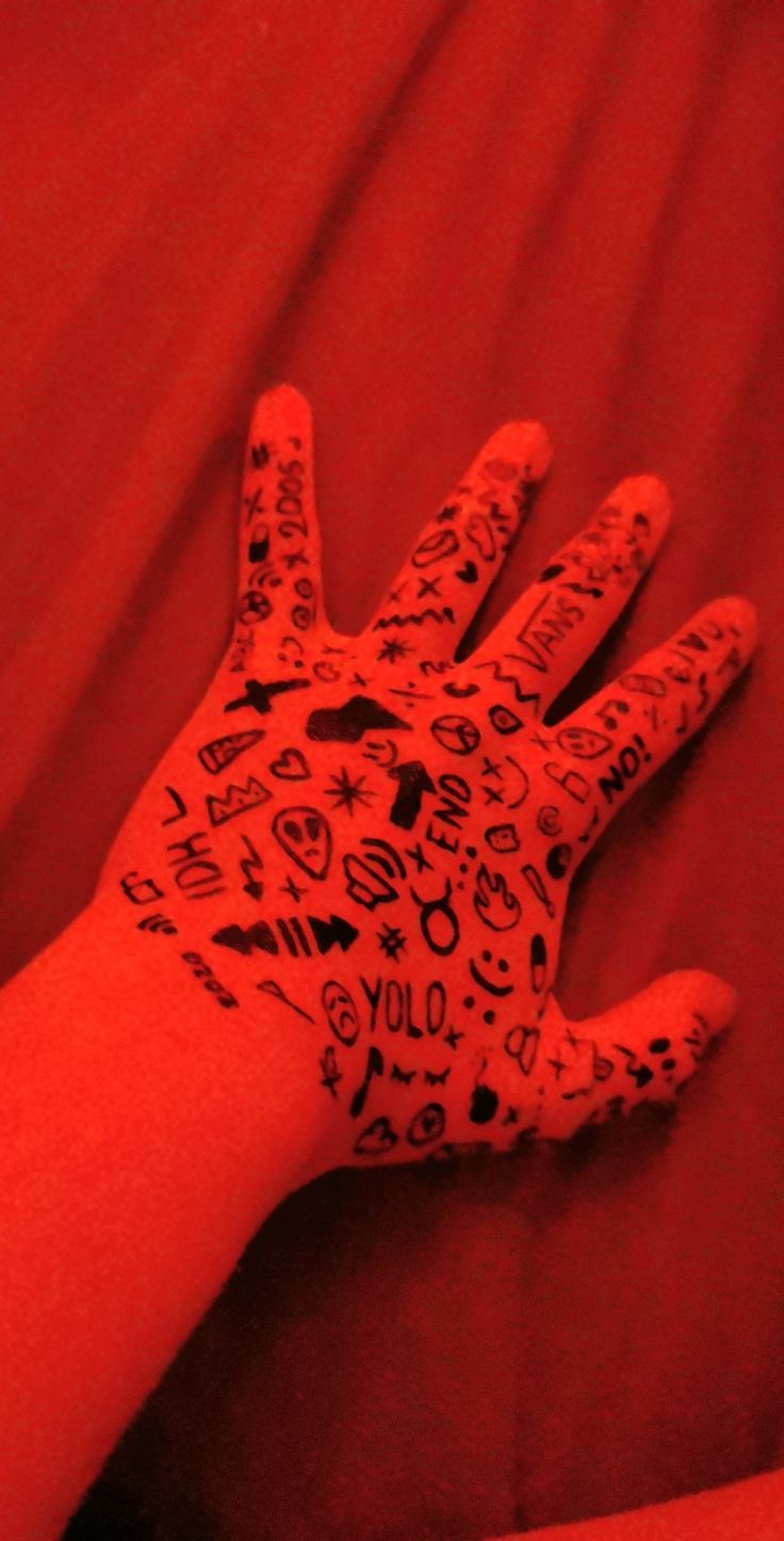 a person's hand covered in black and white drawings on red paper with words written all over it