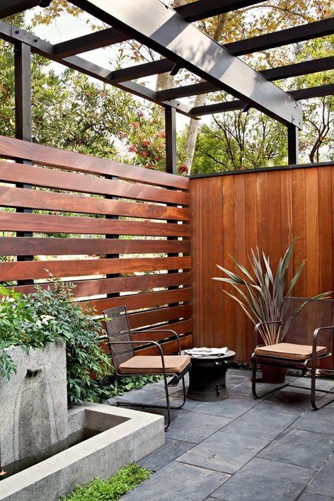 an outdoor patio with two chairs and a planter in the center, next to a wooden fence