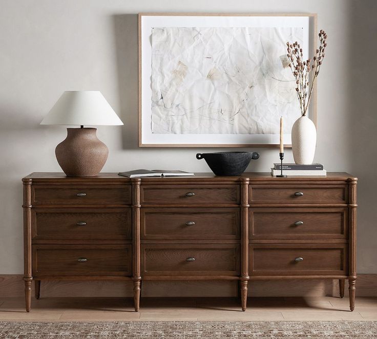 a wooden dresser with two lamps and a painting on the wall in front of it