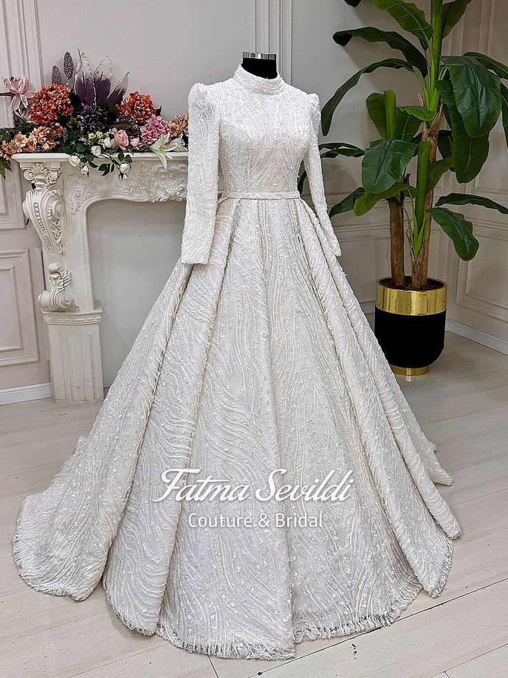 a white wedding dress on display in front of a table with flowers and potted plant