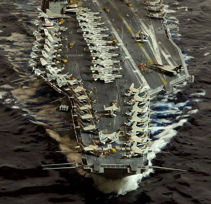 an aircraft carrier in the middle of the ocean with many smaller boats on it's side