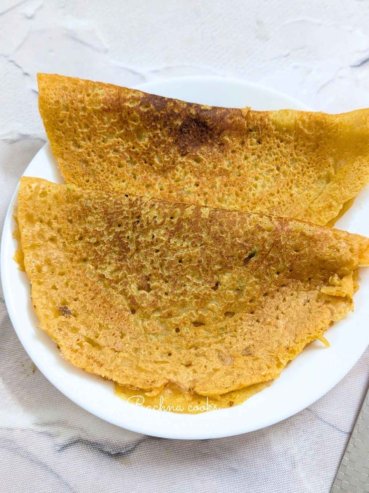 two quesadillas on a white plate sitting on a tablecloth next to a fork