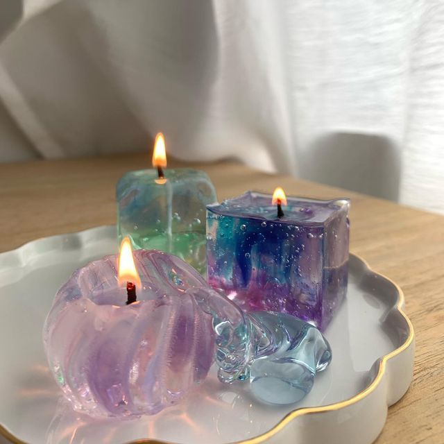 three candles sitting on top of a white plate with purple and green glass cubes