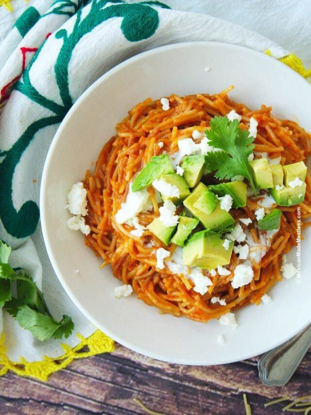 a white bowl filled with spaghetti topped with avocado and feta cheese on top