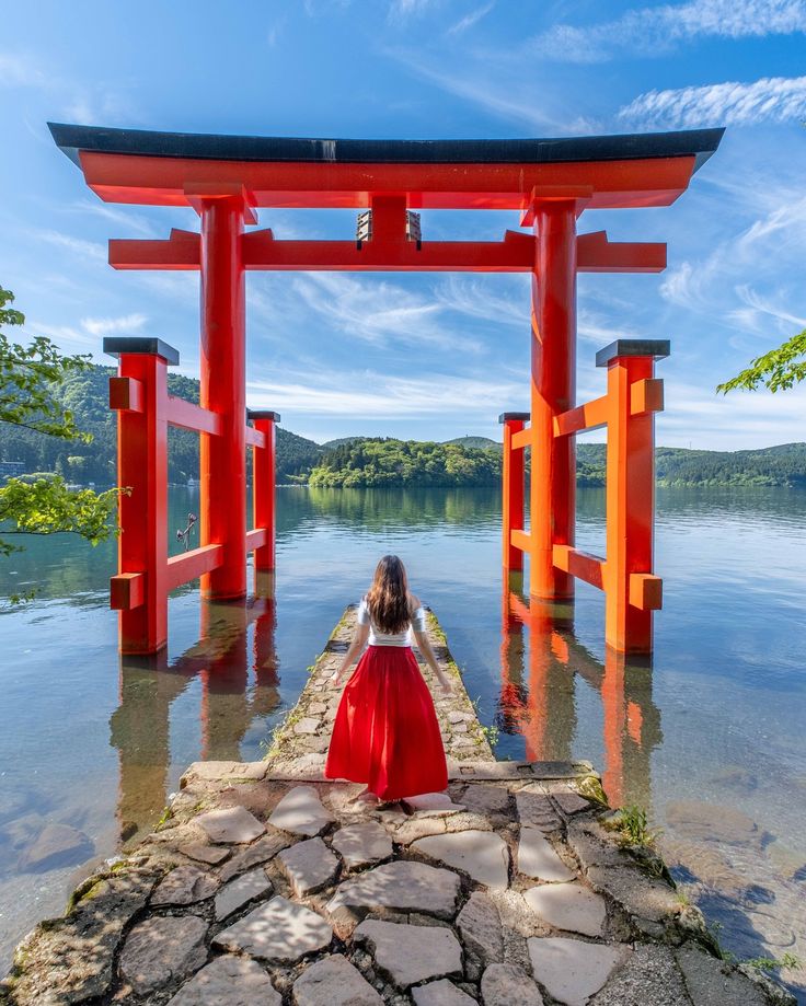 a woman in a red dress is sitting on the edge of a body of water