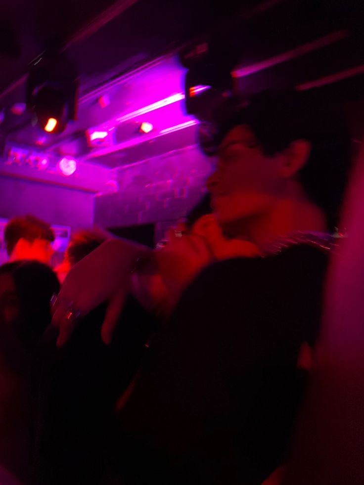 some people are sitting in a dark room with purple lights on the ceiling and one person is holding something up to his ear