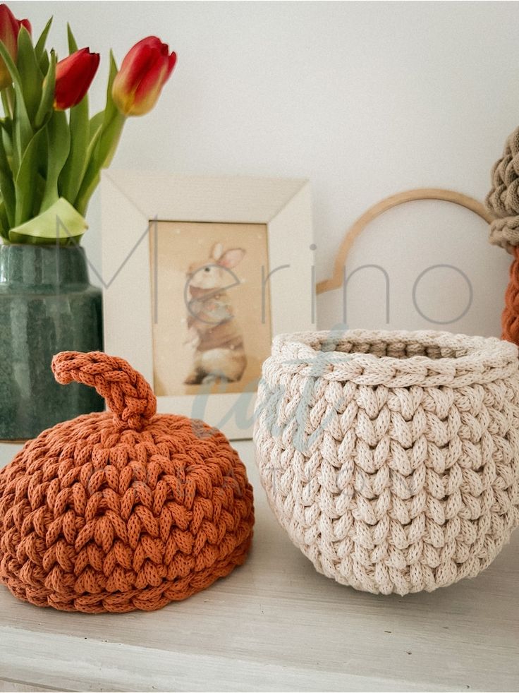 three crocheted pumpkins sitting on a shelf next to tulips in vases