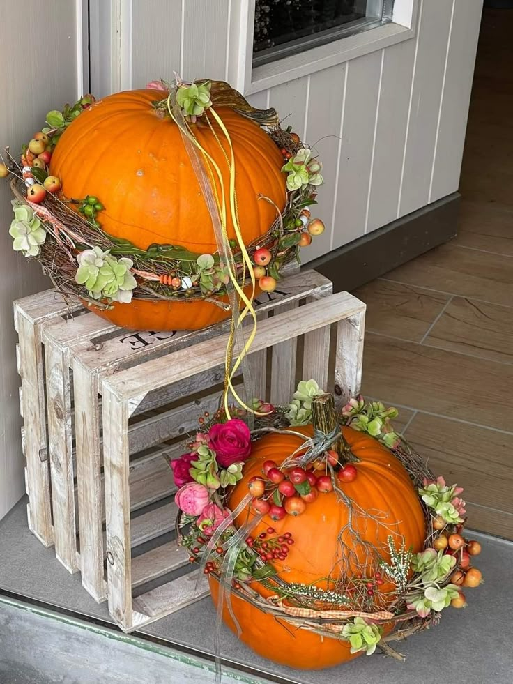 two pumpkins sitting on top of wooden crates with flowers and leaves around them in front of a door