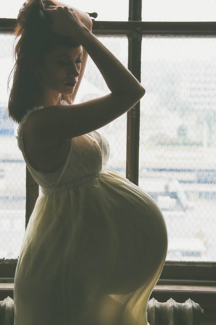 a pregnant woman standing in front of a window with her hands on her head and arms behind her head