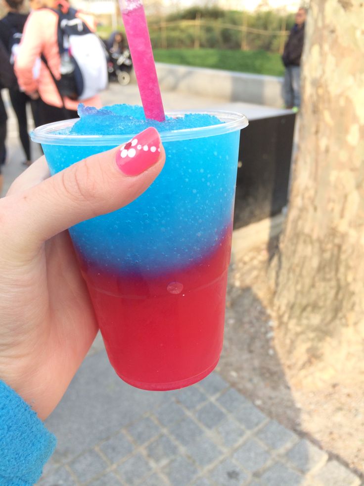 a hand holding a cup with a pink and blue drink in it's middle