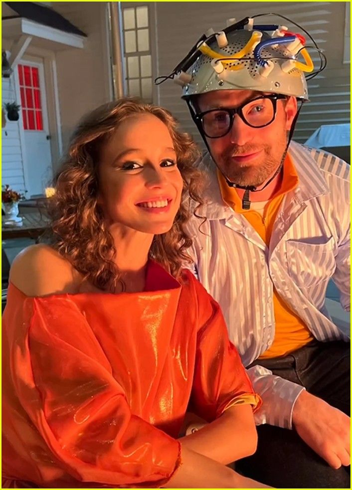 a man and woman sitting next to each other in front of a house with wires on top of their heads