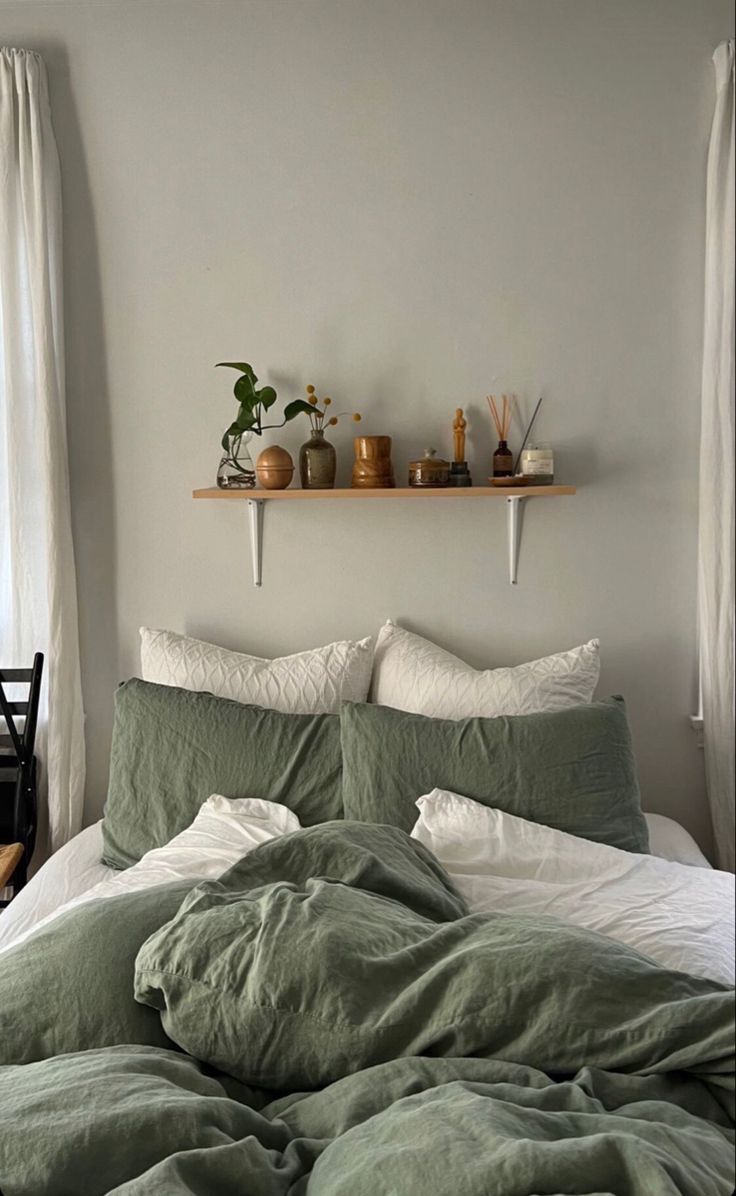 an unmade bed with green linens and pillows in a white room next to a window